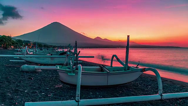 夕阳俯瞰阿贡火山的时间流逝，背景是在海滩上的渔船在阿米德在印度尼西亚的巴厘岛。视频素材