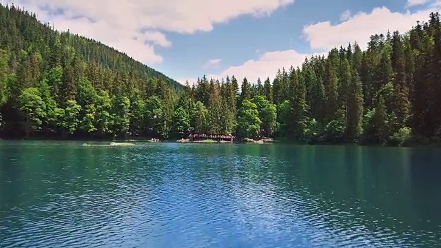 在云杉和松树的群山和森林的背景下，空中飞过美丽的蓝山湖视频素材