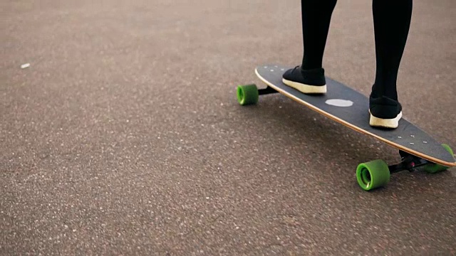 女人的腿在城市的道路上滑板的黑色运动鞋的特写。滑板的腿。Slowmotion拍摄视频素材