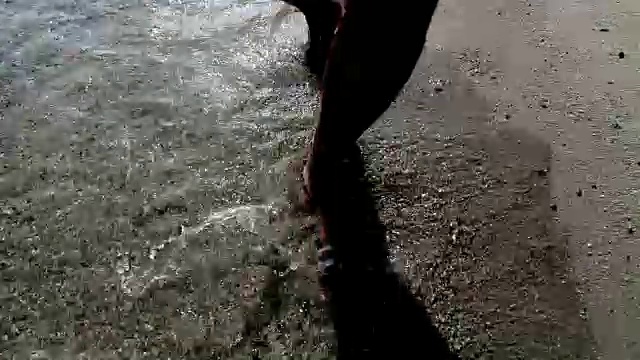 光着脚的男人沿着海岸浅水走着，海浪溅起水花。4k徒步稳定器前视图pov镜头视频素材