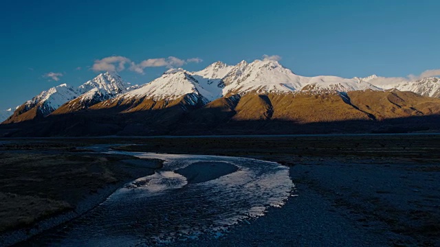 鸟瞰图飞过雪融化的河流，朝向新西兰雪山的山峰视频素材