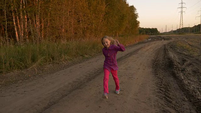 快乐的小女孩在乡村公路上玩，竖起大拇指。一个白人女孩在夕阳下跳起来。视频素材