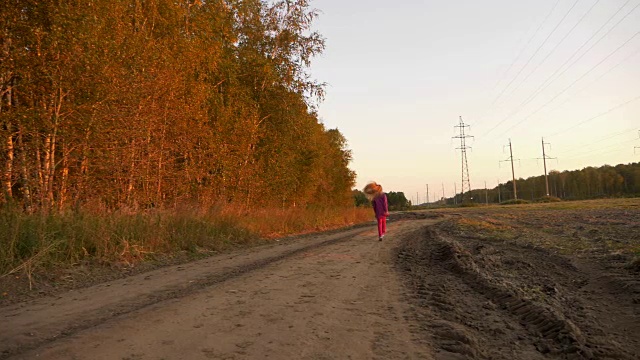 年轻的白人女孩在乡间小路上跳跃奔跑。白色金发的长发女孩在户外跳跃。视频素材