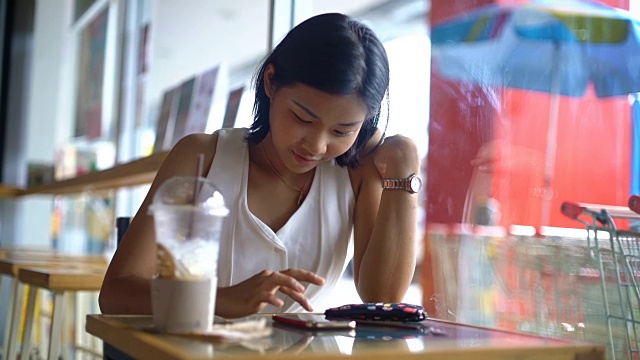 女孩笑着在咖啡店用智能手机打字视频素材