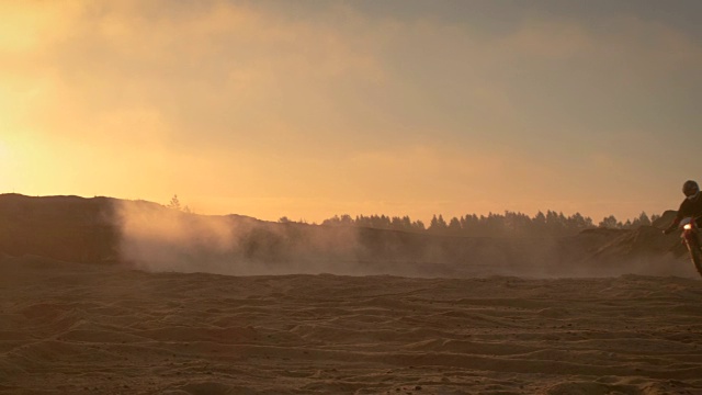 职业摩托车越野赛车手在越野沙地上骑着他的FMX摩托车。夕阳西下，薄雾笼罩大地。视频素材