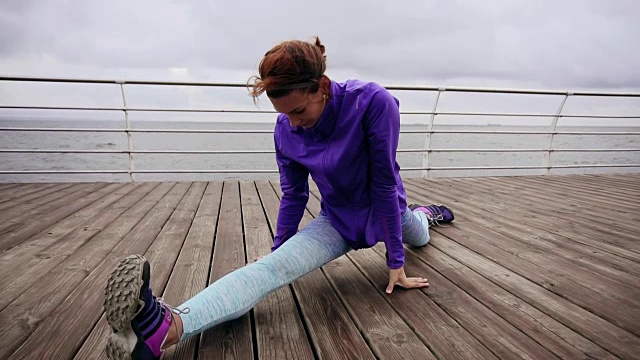 近景:清晨在海边的沙滩上慢跑前，运动女性伸展她的双腿。年轻女孩在做劈叉。夏天在海滩上训练视频素材