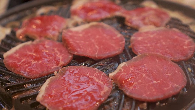 烹饪烧烤，在炉子上的木炭上烤。关闭牛肉烤在日本餐厅。用于烧烤或日式食物的生牛肉片视频素材