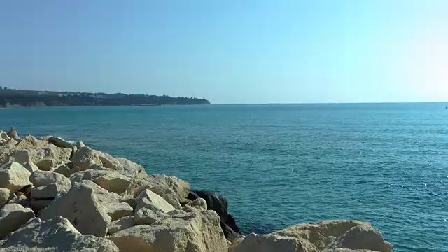 岩石海岸在黑色的海，蓝色的水和天空视频下载