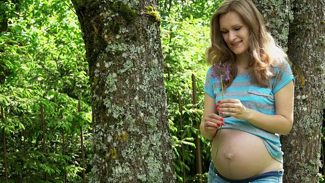 美丽的孕妇与大蒜花抚摸她的肚子在公园视频素材