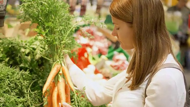 年轻女子在杂货店购物。站在蔬菜区挑选新鲜的胡萝卜视频素材