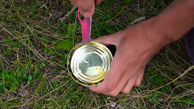 强壮的男子用手打开一个铁罐，用刀在草地上切鱼，在上面拍摄特写镜头。视频素材