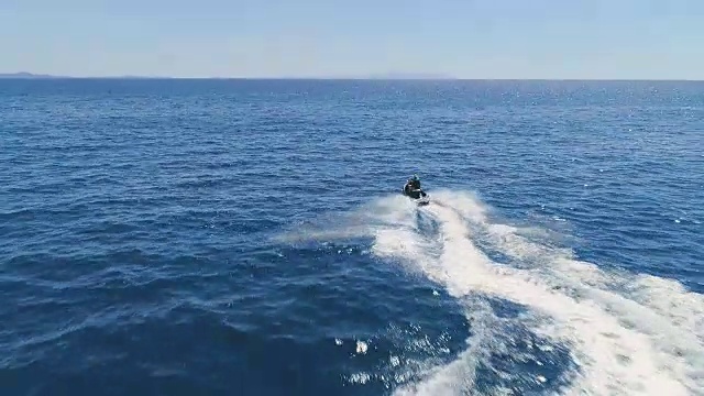 空中跟踪拍摄一对夫妇在一个滑雪喷气机驾驶通过波浪。天气晴朗，海洋是蓝色的。视频素材