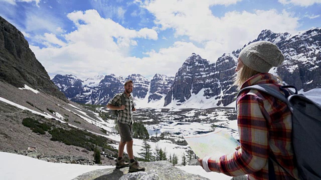 一对年轻夫妇在加拿大的落基山脉徒步旅行，在地图上寻找方向视频素材