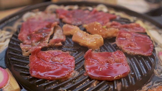 烹饪烧烤，在炉子上的木炭上烤。关闭牛肉烤在日本餐厅。用于烧烤或日式食物的生牛肉片视频素材