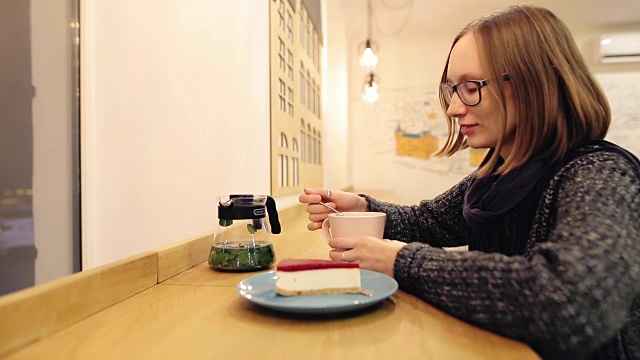 Сheerful女孩享受一杯热饮料和甜点坐在晚上在咖啡馆。迷人的白种女人戴着好心情的玻璃杯喝薄荷茶，肉桂，酸橙和蜂蜜视频素材