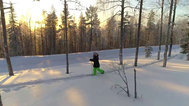 在金色的冬日夕阳下，女孩穿着雪鞋在厚厚的雪地上徒步行走视频素材