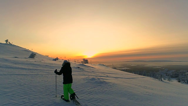 空中镜头:冬天日出时，飞向穿着雪鞋在雪山上徒步旅行的女人视频素材