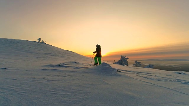 在冬天，穿着雪鞋的女性在粉红色的晚霞中徒步旅行视频素材