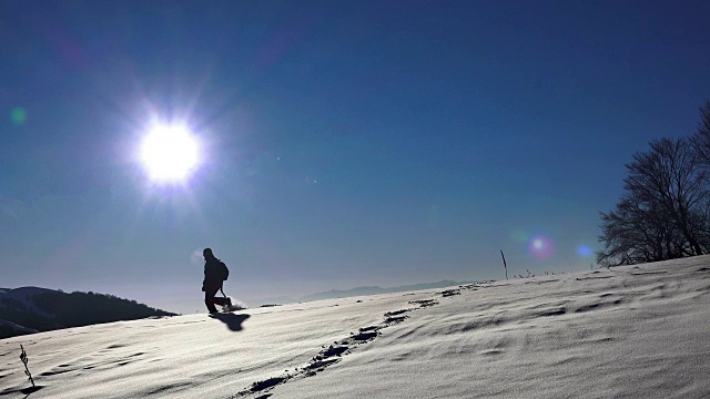 在雪地里行走的徒步旅行者。探险的旅程。脚脚陡峭。雪的冬天。体育娱乐活动。太阳背光的剪影在地平线上。超高清4K库存素材视频素材