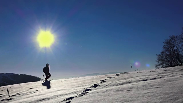 在雪地里行走的徒步旅行者。探险的旅程。脚脚陡峭。雪的冬天。体育娱乐活动。太阳背光的剪影在地平线上。超高清4K库存素材视频素材