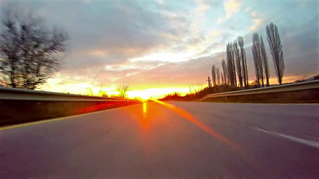 在乡村道路上行驶的跑车夕阳。车轮旋转POV -观点，日出。旁边有树。运动速度快。4 k拍摄视频素材