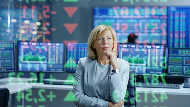 股票市场女性高级经理看着预测的股票号码和图表。在她满是屏幕和数据的房间后面。视频素材