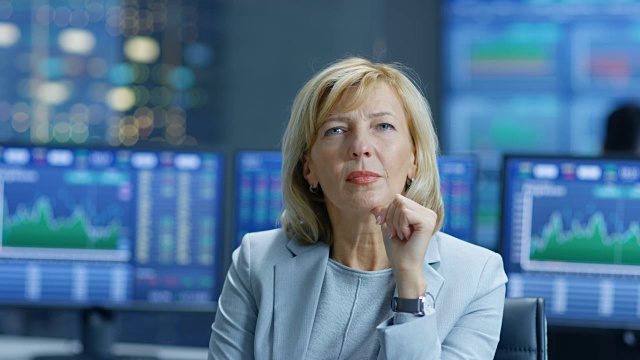 股票市场领先分析师努力思考解决财务问题。在她的背后，人们工作和显示器显示图形和股票数字。视频素材
