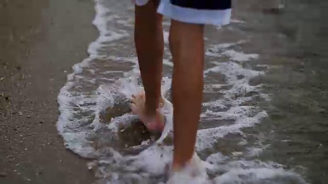 小男孩沿着金色的沙滩走着，镜头拉近了双脚视频素材