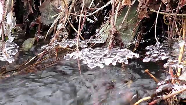 一条美丽清澈的小河从积雪中流淌而出，声声融解。流动的水形成了有趣的形状，因为它在原始的冰晶，4k冬季背景视频素材