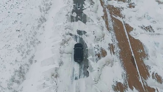 一辆黑色汽车行驶在雪地里的乡村道路上，无人机拍摄的鸟瞰图视频素材