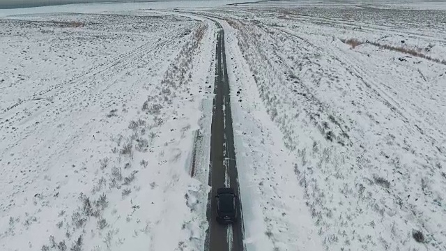 一辆黑色汽车行驶在雪地里的乡村道路上，无人机拍摄的鸟瞰图视频素材