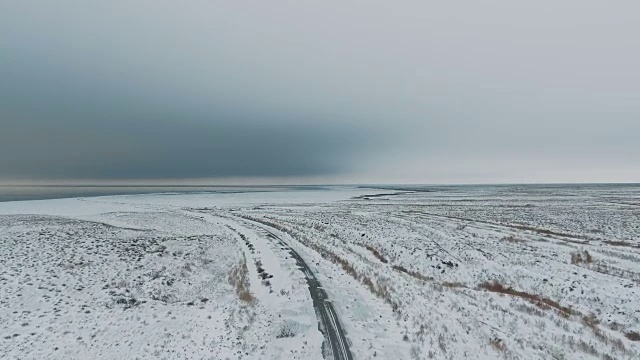 一辆黑色汽车行驶在雪地里的乡村道路上，无人机拍摄的鸟瞰图视频素材