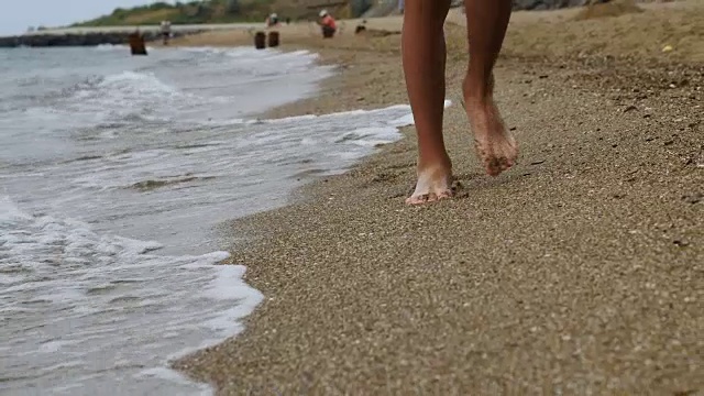 男孩在海滩上的金色沙滩上走着，拿着手机视频素材