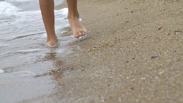 男孩在海滩上的金色沙滩上走着，拿着手机视频素材