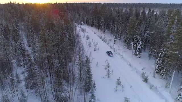 空中镜头:在冬日金色的日出中，汽车在白雪覆盖的森林中行驶视频素材