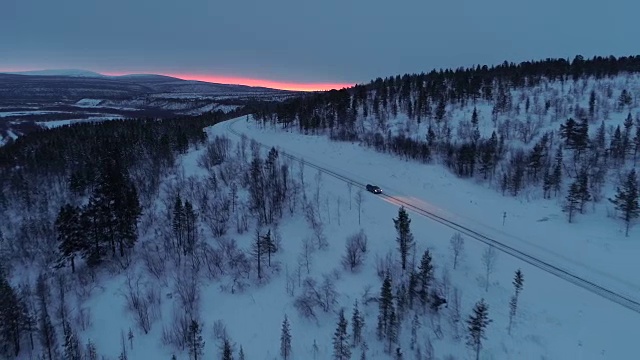 日落时分，一辆汽车在雪山路上穿过云杉林视频素材