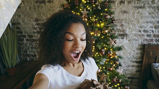 有趣的混血女孩在圣诞树旁用智能手机自拍视频素材