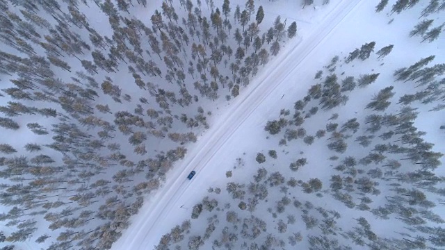 空中俯瞰:汽车行驶在积雪的道路上，穿过寒冷的冬季松林视频素材