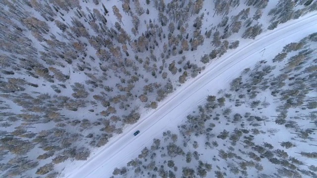 空中俯瞰:汽车行驶在积雪的道路上，穿过寒冷的冬季云杉森林视频素材