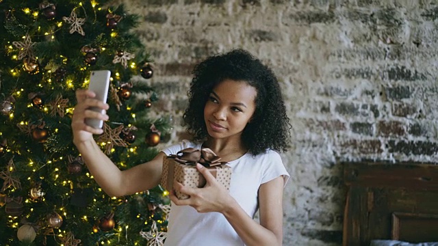有趣的混血女孩在圣诞树旁用智能手机自拍视频素材