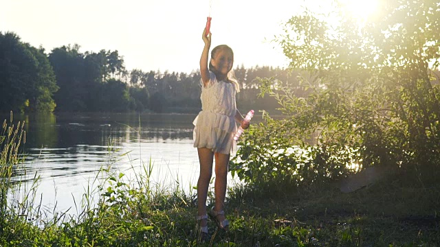 小女孩拿着泡泡棒在湖岸上跳。视频素材