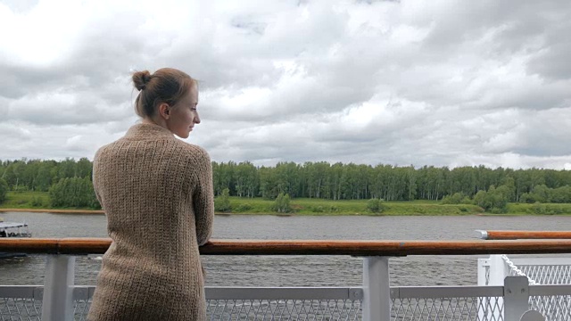 年轻女子站在游轮的甲板上，看着河流和风景视频素材