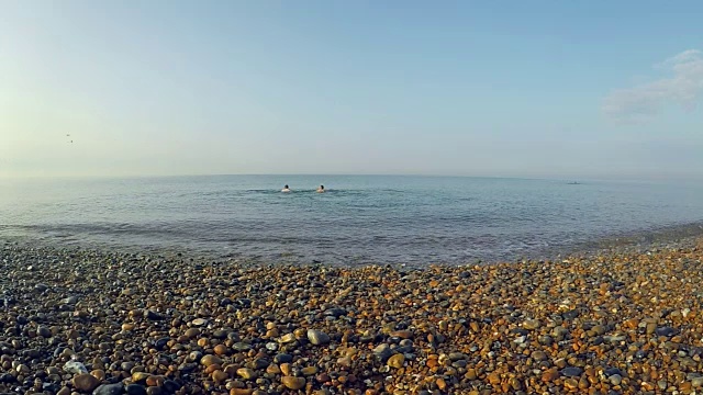 平静的海面上，小波浪拍打着卵石滩，游泳者可见视频素材