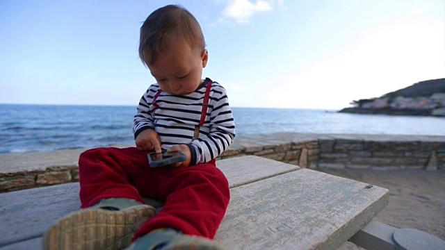 一个小男孩正在海滩上玩手机视频下载