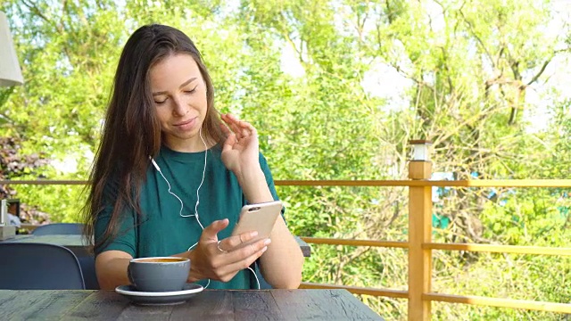 一名年轻女子在空闲时间独自坐在咖啡店里用手机打电话。迷人的女性与可爱的微笑交谈与手机，而休息在咖啡馆视频素材