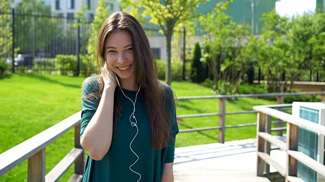 年轻女子戴着耳机听音乐。迷人的女性与可爱的微笑与手机，而休息在咖啡馆视频素材