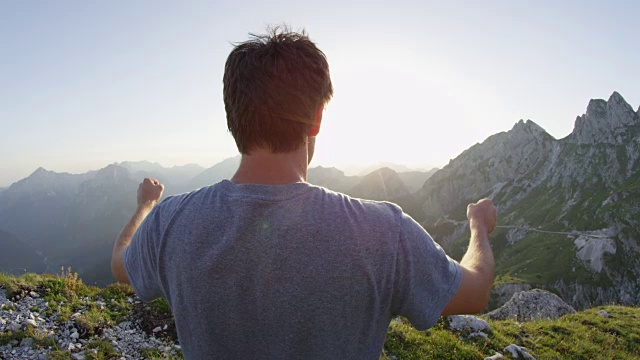 近距离镜头光晕:年轻的男性徒步旅行者在到达山顶后举起双臂。视频素材