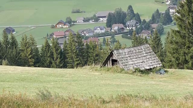 舒适的非常古老的木屋在奥地利阿尔卑斯山的一个小山上，绿色的草在新的现代房子的背景，古老的乡村木屋在村庄视频素材