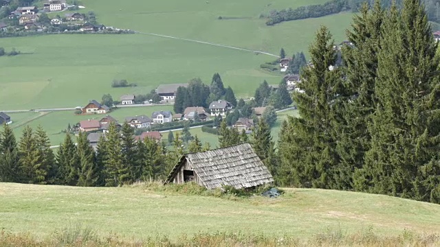 舒适的非常古老的木屋在奥地利阿尔卑斯山的一个小山上，绿色的草在新的现代房子的背景，古老的乡村木屋在村庄视频素材