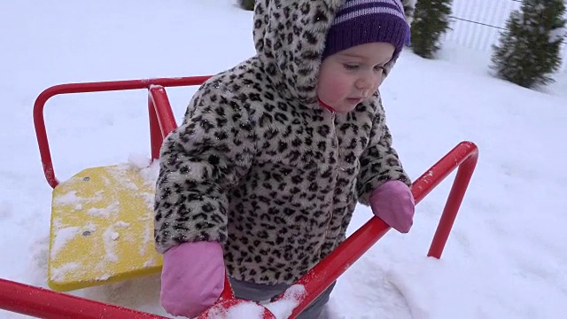 大雪纷飞的冬天，小女婴在操场上荡秋千。FullHD视频素材